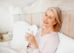 Cheerful mature female holding coffee mug in bed